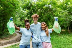 Happy community service people cleaning up local park. They have a trash bag and are filling is with trash they have found in the park. Their are two knealing down and two others behind them photo