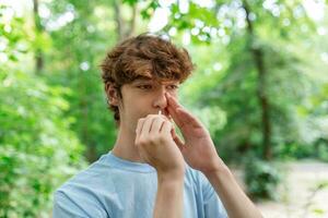 joven hombre es utilizando nasal rociar debido a el problemas con nariz y respiración en el público parque. foto