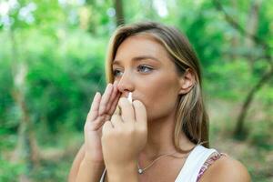Woman using nasal spray outdoors for tree pollen allergy treatment photo