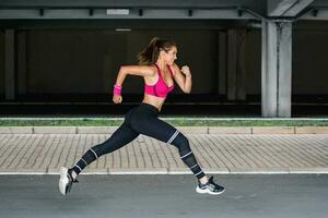 Young woman with fit body jumping and running against grey background. Female model in sportswear exercising outdoors. photo