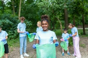 The young adult woman, who is one of a diverse group of volunteers, takes time to smile for the camera. Hold garbage bag and looking at camera photo