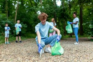 Happy community service people cleaning up local park. They have a trash bag and are filling is with trash they have found in the park. Man knealing down and others behind them photo