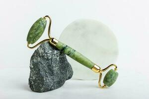 Green jade roller massager for face on white marble. photo