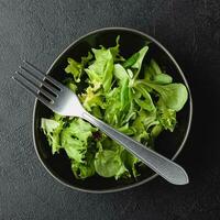 hojas de ensalada verde en un tazón sobre una mesa negra. foto