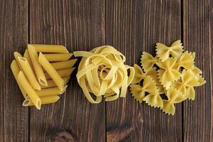 Different kinds of raw pasta on wooden background. photo