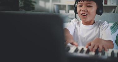 muñequita disparo, creativo asiático chico vistiendo auricular con artístico habilidades tomando música lecciones en línea durante un vídeo llamada y jugando el piano a hogar. música, pasatiempo y estilo de vida conceptos. video