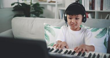 Handheld shot, Creative asian boy wearing headphone with artistic skills taking music lessons online during a video call and playing the piano at home. Music, hobby and lifestyle concepts.