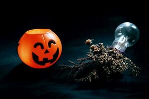 Halloween pumpkin head with dry flowers in vase glass on black clothes in natural shadow and light. Halloween holiday concept. photo