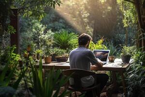 a man sitting on a table outside using a laptop in a garden with photo