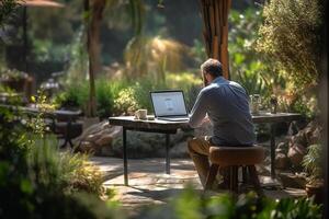 a man sitting on a table outside using a laptop in a garden with photo
