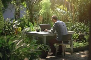 a man sitting on a table outside using a laptop in a garden with photo