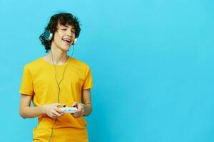 curly guy plays with joystick in yellow t-shirts blue background photo