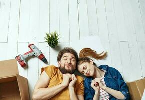 man and woman with boxes around lie on the floor moving flower in a pot repair work photo