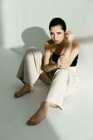 barefoot woman sitting on the floor leaning against the wall indoors pants style suit photo