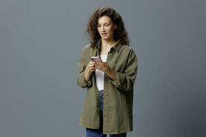 Shocked excited confused curly beautiful woman in casual khaki green shirt get shock info from message using phone posing isolated on gray blue background. Social Media Influencer concept. Copy space photo