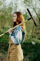 A woman farmer in work clothes and an apron works outdoors in nature and holds a rake to gather grass photo