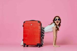 woman tourist with red suitcase wearing sunglasses fun pink background photo