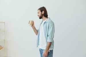 Lanza libre milenario hombre con barba Bebiendo café desde un cangrejo taza en elegante hipster ropa en un blanco antecedentes foto