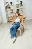 Cheerful young blonde lady in warm sweater in headphones listen enjoy fav songs dancing sitting in armchair at modern home interior. Music time Relaxing Cool playlist Concept. Copy space photo