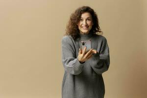 Overjoyed lucky curly cute lady in gray casual sweater get cool news from message posing isolated on over beige pastel background. Social media, network, distance communication concept. Copy space photo