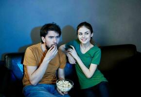 energético mujer modelo en un cuero sofá y un hombre palomitas de maiz en un noche plato foto