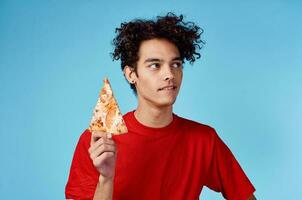 energético chico con un rebanada de Pizza teniendo divertido en un azul antecedentes y un rojo camiseta foto