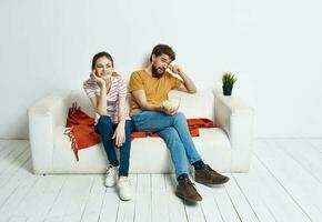 un hombre y un mujer en un blanco sofá en un brillante habitación un plato de palomitas de maiz y amigos un flor en un maceta foto