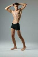 athlete in black shorts holds hands behind his head naked torso gray room full-length model Copy Space photo