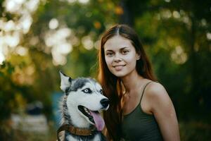 un mujer con un fornido raza perro sonrisas y afectuosamente golpes su amado perro mientras caminando en naturaleza en el parque en otoño en contra el fondo de puesta de sol foto