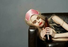 mujer con botella de cerveza en sofá alcohol adiccion dormir máscara en cabeza foto
