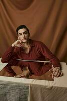 Handsome guy in a shirt posing at a table indoors on a fabric background and a square mirror photo