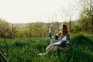 A young, beautiful woman lounges on the green grass in the park wearing sneaker pants and a plaid shirt and looks out into the setting sun photo