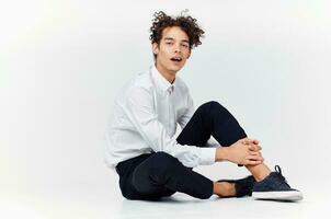 man with curly hair in a classic suit and sneakers sits on the floor and side view Copy Space photo