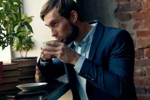 un hombre en un traje bebidas café cerca el ventana de un cafetería. foto