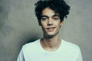 contento adolescente en blanco camiseta Rizado pelo riendo sonrisa beige antecedentes fotografía estudio foto