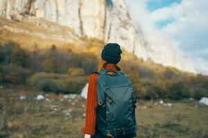 woman in a warm hat with a backpack on her back and in a sweater outdoors in the mountains gesticulate with her hands photo
