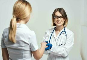 el enfermero batidos manos con el paciente en un ligero antecedentes y azul guantes con un estetoscopio foto