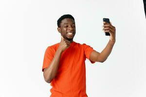 happy guy of african appearance in an orange t-shirt with a mobile phone photo