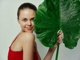 smiling woman holding green leaf in her hands red swimsuit light background photo