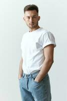 Portrait shot of handsome pensive romantic serious tanned man guy in basic t-shirt looks at camera posing on white background. Fashion Style New Collection Offer. Copy space for ad. Model snap photo
