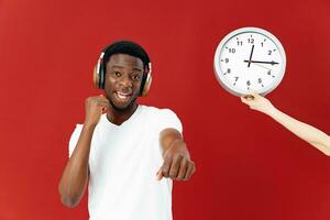 hombre de africano apariencia en auriculares gesticulando con su manos siguiente a el reloj foto