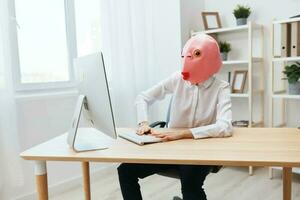 Focused funny crazy businesswoman worker freelancer in pink fish mask work on computer online pondering or making decision thinking of problem solution in light modern office. Copy space photo