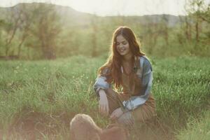 Young redheaded woman playing in nature with her dog in sunny park at sunset in summer photo