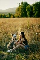 Woman sitting in field with dachshund dog smiling while spending time in nature with friend dog in autumn at sunset while traveling photo