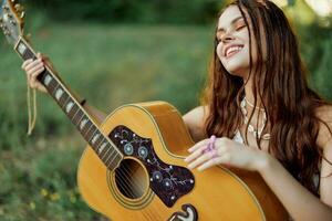 Young hippie woman with eco image smiling and looking into the camera with guitar in hand in nature on a trip photo