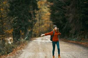 happy woman hiker with backpack walks on the road in autumn forest photo