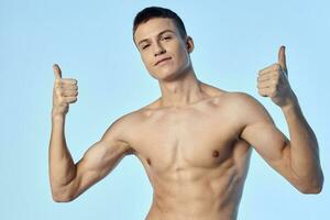 sporty man with naked torso showing thumb on blue background photo