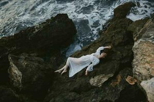 sensual woman in a secluded spot on a wild rocky coast in a white dress Summer vacation concept photo