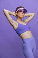 Athletic fashion woman posing in a purple sports suit for yoga and a transparent cap on a purple background monochrome photo