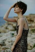 short haired woman in shiny dress posing near rocks photo